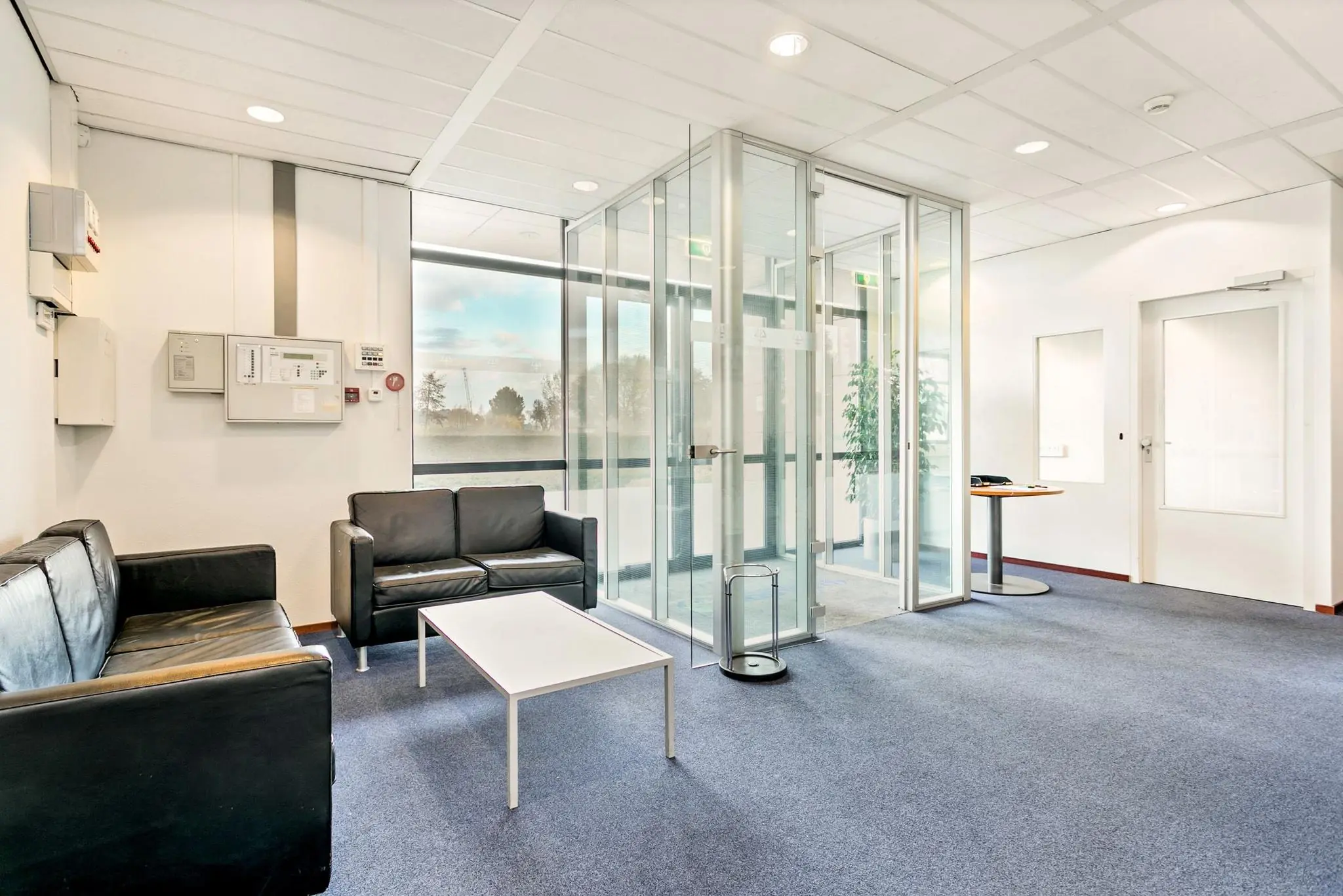 Moderne wachtruimte op Laan van S-Gravenmade met zwarte leren banken, glazen entree en veel daglicht.